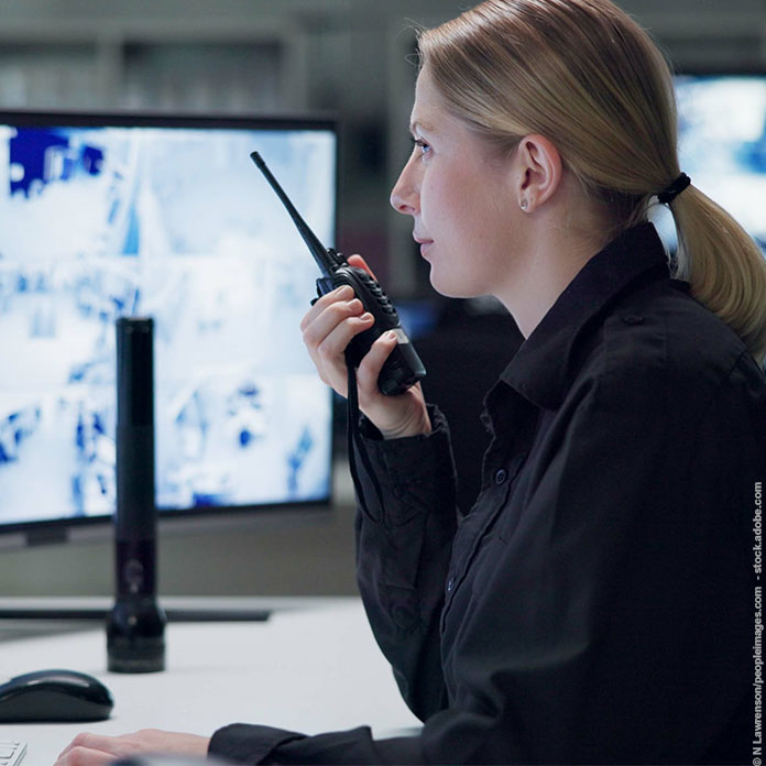 Mitarbeiterin einer Sicherheitsfirma mit Funkgerät vor Monitoren
