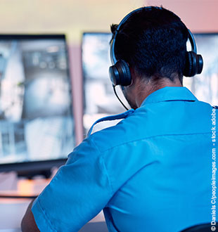 Sicherheitsmann mit Kopfhörern vor Überwachungs-Monitoren