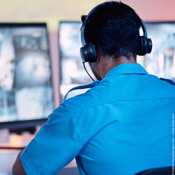 Mitarbeiterin einer Sicherheitsfirma mit Funkgerät vor Monitoren