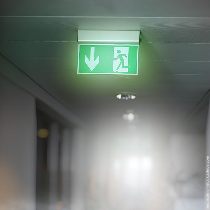 Büroflur mit Rauch und einem beleuchteten Exit-Schild an der Decke