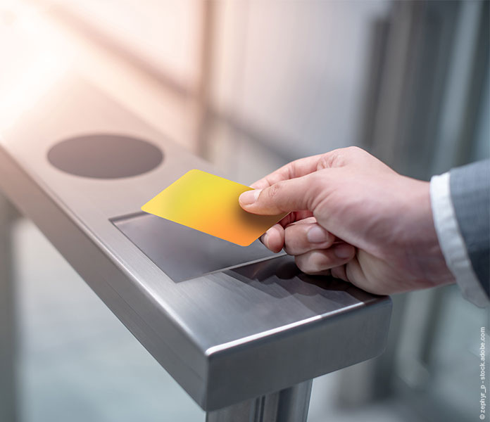 Hand eines Geschäftsmannes, der eine gelbe Smartcard benutzt, um ein automatisches Tor in einem Bürogebäude zu öffnen.